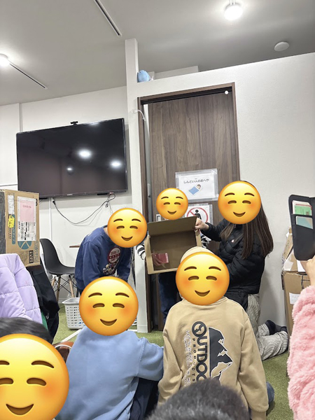 放課後等デイサービスの児童が段ボールの中に手を入れ、何が入っているか当てるゲームをあいています。