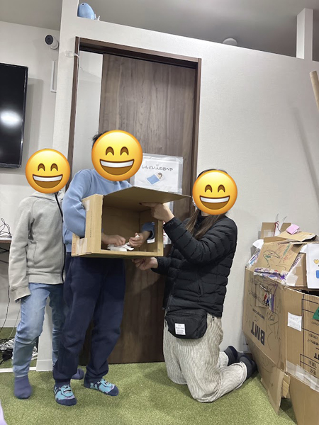 放課後等デイサービスの児童が段ボールの中に手を入れ、何が入っているか当てるゲームをあいています。